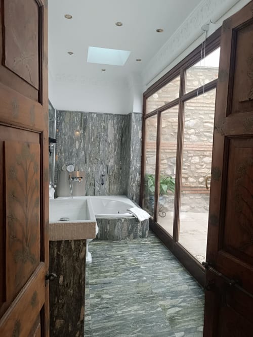 Baño moderno en Suite Comares Granada con azulejos de pizarra verde, bañera profunda y puertas de cristal hacia el patio