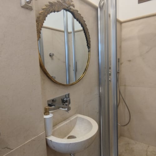Baño compacto en Suite Comares Granada con espejo ovalado, lavabo mural y cabina de ducha