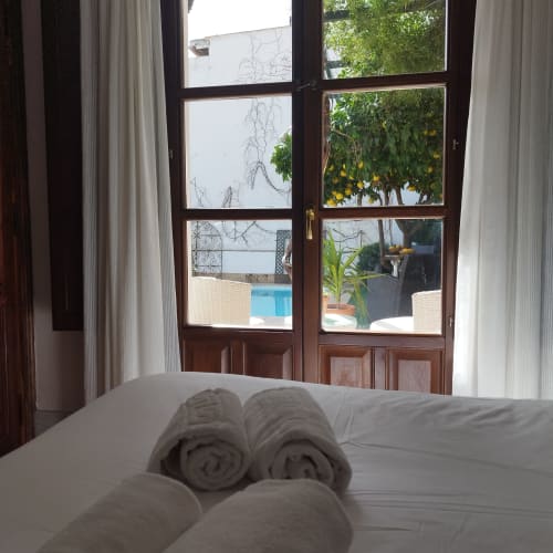Toallas enrolladas en la cama con puertas abiertas hacia la piscina y jardín del hotel Suite Comares en Granada