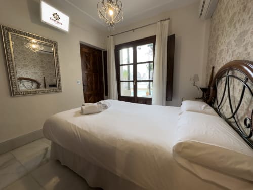 Dormitorio luminoso en la Suite Comares del hotel de Granada con camas gemelas, espejo ornamentado y puertas de balcón con vistas a la piscina