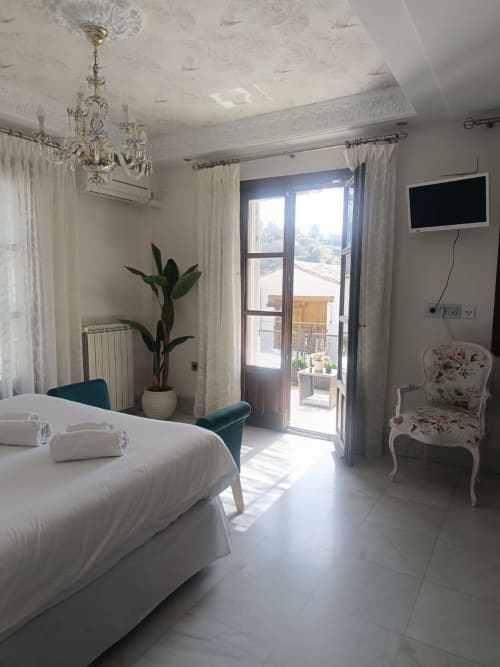 Elegante habitación de hotel en Suite Comares Granada con cama blanca, lámpara de cristal y balcón con vistas al monumento