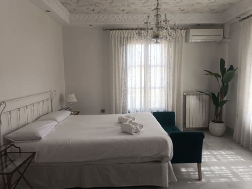Dormitorio luminoso y elegante en el hotel Suite Comares de Granada con ropa de cama blanca, araña de cristal y vistas al balcón