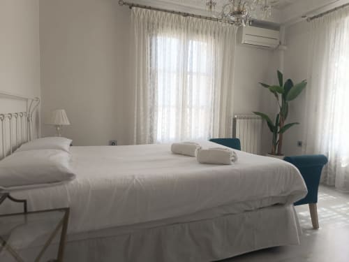 Dormitorio moderno y luminoso en Suite Comares de Granada con ropa de cama blanca, cortinas translúcidas y planta junto a la ventana