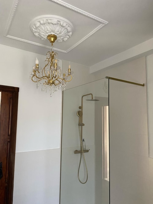 Elegante cuarto de baño en Suite Comares Granada con lámpara de araña de bronce, medallón de techo ornamentado y moderna mampara de ducha de cristal