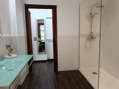 Baño moderno en Suite Comares de Granada con lavabo turquesa, piso de azulejos oscuros y ducha de obra con mampara de cristal