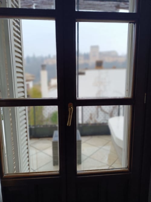 Puertas con marco negro abiertas a la vista del paisaje urbano de Granada desde el balcón de la Suite Comares