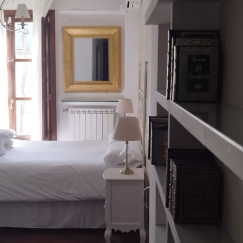 Dormitorio Suite Comares Granada con ropa de cama blanca, espejo dorado, radiador y decoración clásica