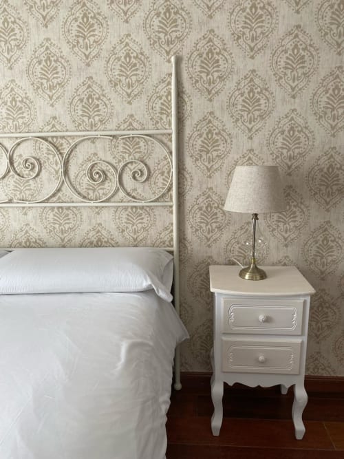 Elegante habitación de la Suite Comares Granada con papel tapiz de damasco ornamentado, cabecero de hierro blanco y lámpara de latón