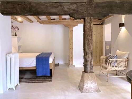 Amplio dormitorio rural en Casa MAÑARINEGI con vigas de madera vista, paredes blancas, cama de madera con manta azul, silla de mimbre,