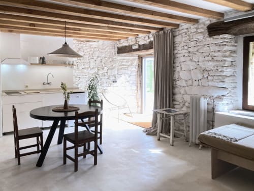 Estudio rústico luminoso en Gipuzkoa con muros de piedra vista, vigas de madera, mesa de comedor, cocina americana y cama con vistas al jardín