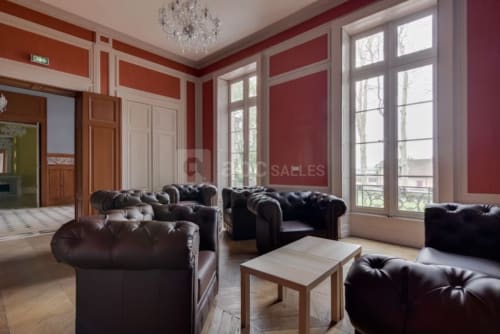 Élégant salon de l'auberge La Maison Verneuil à Paray-le-Monial avec murs bordeaux, fauteuils Chesterfield en cuir et grandes