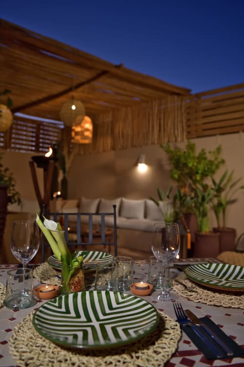 Evening dinner setup at Riad Palau Marrakech with green striped plates, candles, and wine glasses under wooden pergola