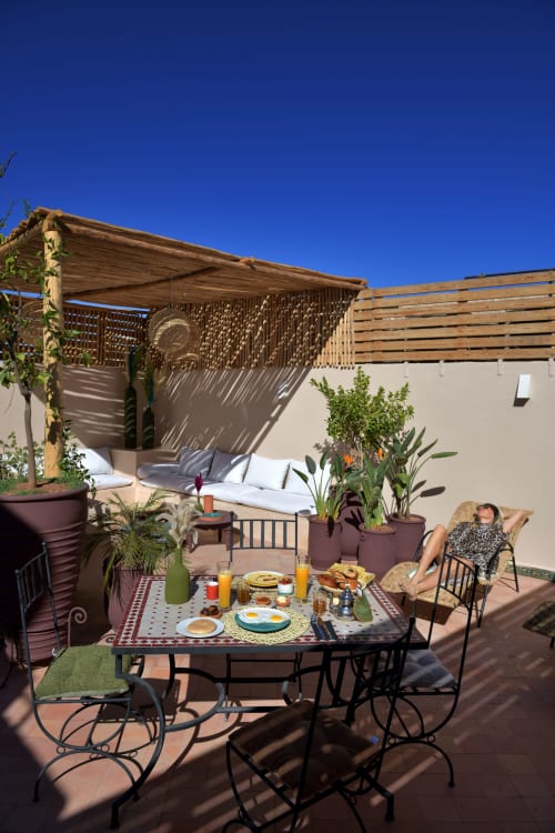 Sunny terrace at Riad Palau Marrakech with breakfast table, wooden pergola, and lounge seating