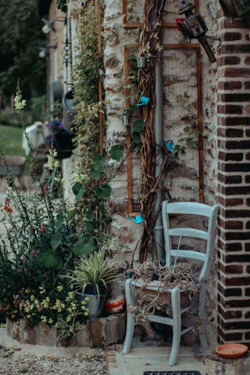 Cour rustique du Clos du Buisson avec chaise blanche, lierre grimpant et fleurs en pots
