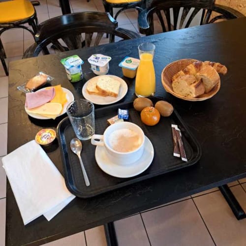 Table de petit-déjeuner à l'hôtel Les Deux Porches avec café, viennoiseries, fromage, jambon, jus et fruits à Verrières.