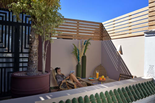 Vrouw ontspant zich op een loungestoel op het zonnige terras van Riad Palau Marrakech met houten pergola en potplanten