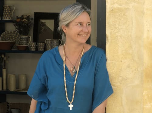 Femme souriante à la Dragonne B&B à Bellême, France, portant un chemisier bleu et un collier de perles près d'une décoration rustique