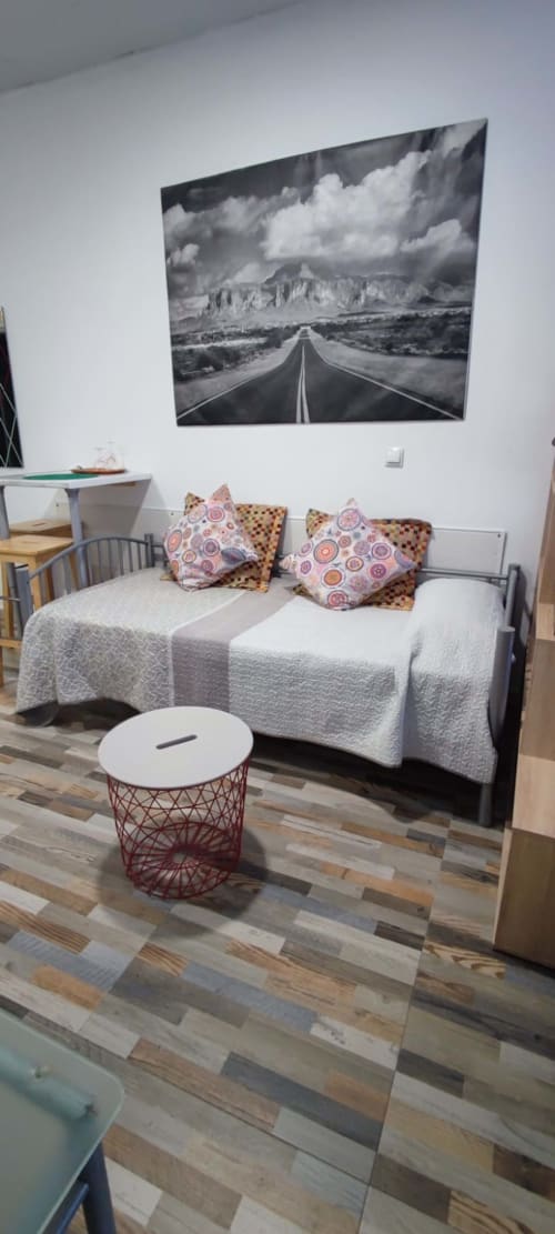 Dormitorio moderno en apartamento de Huelintown Málaga con cama, cojines decorativos y obra de arte de carretera desértica