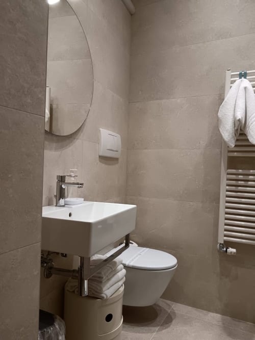 Modern bathroom at Stella CasaBono hotel in Sulmona with white sink, toilet, curved mirror, towel rack, and neutral tile
