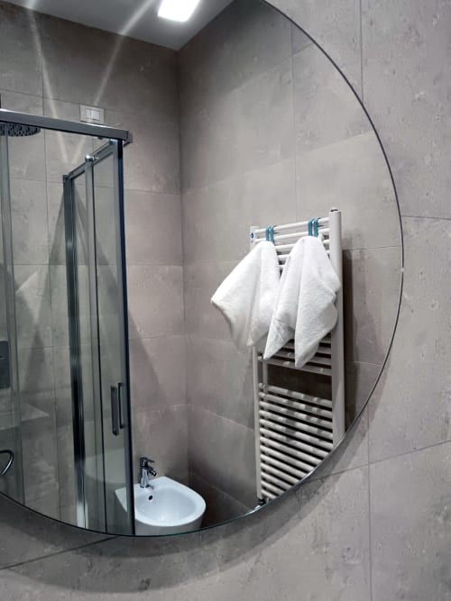 Modern bathroom in Stella CasaBono hotel with curved glass shower enclosure, white heated towel rack, and gray tile walls