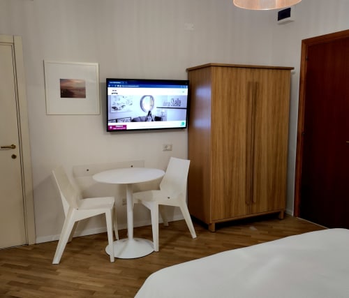 Modern hotel room at Stella CasaBono with white dining table, wooden wardrobe, wall-mounted TV, and wood flooring