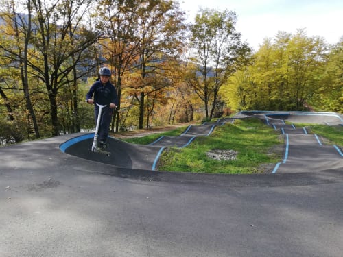 Child riding electric scooter at outdoor skate park near Aime la Plagne, autumn forest setting