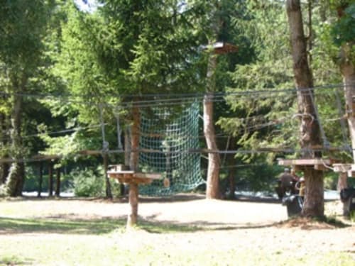 Outdoor adventure park with rope course and zipline surrounded by tall pine trees at La Maison De L'Épine in Aime la Plagne