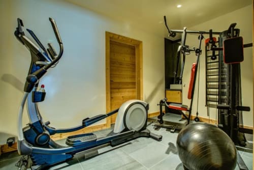 Home gym at Le Chalet Mont-Blanc with elliptical, exercise bike, weight machine, and fitness ball in Chamonix