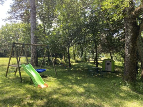 Aire de jeux extérieure du Domaine de Bize avec toboggan vert, balançoire et siège bleu parmi les arbres à Mirepoix, Ariège