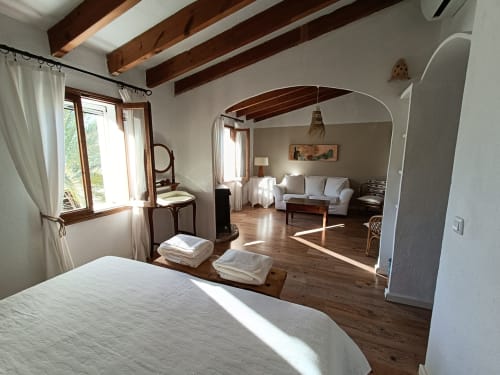 Amplia suite Xaloc del Petit Hotel Sa Plana en Estellencs con vigas de madera, zona de estar y vistas al jardín
