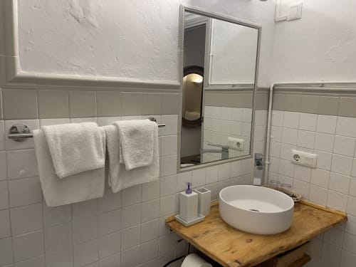 Baño moderno en Petit Hotel Sa Plana con paredes de azulejos blancos, lavabo redondo sobre mueble de madera, espejo y toallas blancas
