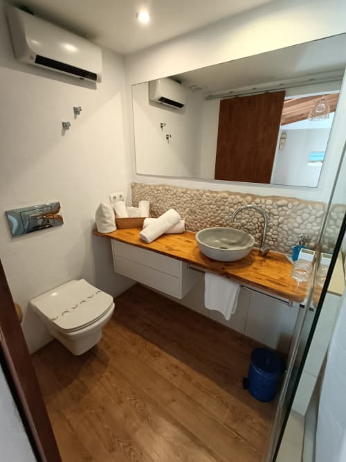 Baño moderno del Petit Hotel Sa Plana con mueble de madera, lavabo redondo, revestimiento de piedra y ducha en Estellencs