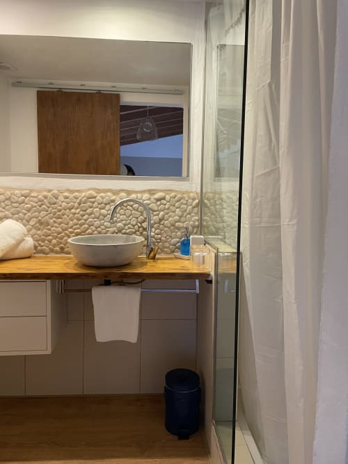 Baño moderno en Petit Hotel Sa Plana con lavabo de cerámica blanca, mueble de madera, azulejos texturados y ducha de cristal