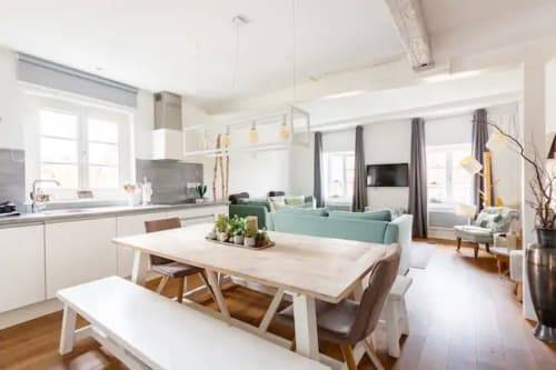 Cucina moderna a pianta aperta e sala da pranzo con mobili bianchi, tavolo in legno e divano verde menta nell'appartamento di Colmar.
