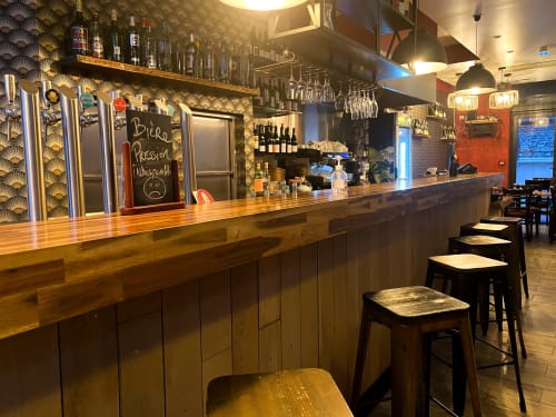 Comptoir de bar moderne à l'hôtel Chambre Pasteur à Montreuil avec sièges en bois, alcools en rayons et éclairage contemporain