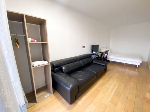 Chambre spacieuse Pasteur Montreuil avec canapé cuir noir, lit blanc, étagères bois et parquet