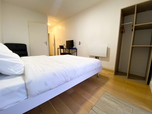 Spacieuse chambre de l'hôtel Chambre Pasteur à Montreuil avec lit blanc, bureau, armoire et parquet