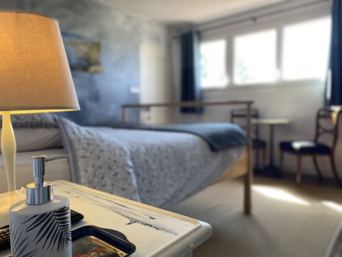 Bright bedroom at L'Ermitage B&B in Saint-Vaast-la-Hougue with lamp, bed, windows, and chair