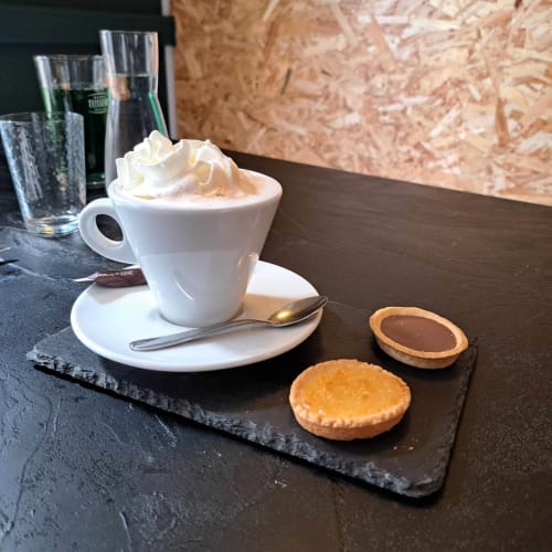 Cappuccino avec crème fouettée et pâtisseries à l'hôtel Les Deux Porches à Verrières, servis sur ardoise avec verres d'eau.