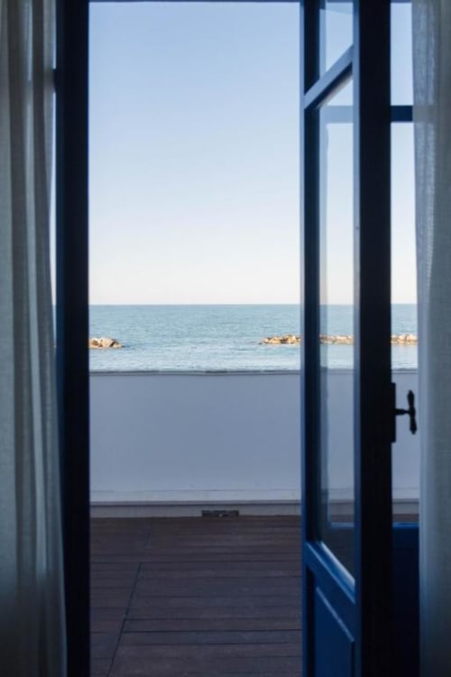 Porte in vetro aperte che rivelano il balcone con vista sul mare a Le Vajane, Torino di Sangro, con costa rocciosa e orizzonte visibili