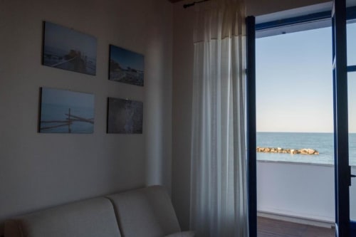 Camera costiera luminosa con vista mare attraverso porte aperte, tende di lino bianco e fotografie costiere a Le Vajane, Torino di