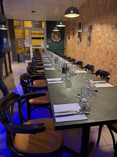 Salle à manger moderne du restaurant Les Deux Porches avec table longue, chaises noires, murs en liège, luminaires suspendus et touches vintage