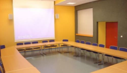Salle de conférence moderne de l'hôtel Les Deux Porches à Verrières avec murs jaunes, table en U et écran de projection