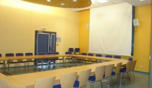 Salle de conférence moderne de l'hôtel Les Deux Porches à Verrières avec murs jaunes, table courbe et chaises bleues