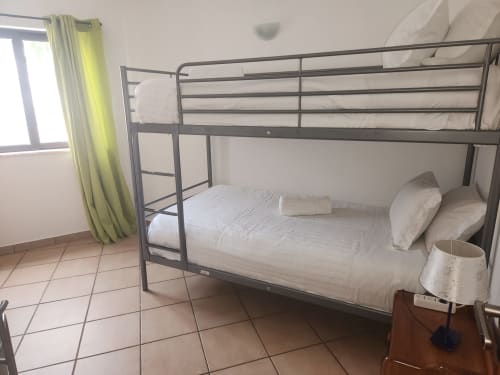Cama beliche de metal com roupas de cama brancas no quarto Twin Econômico da pousada Sunny House em Lagos, cortinas amarelas e piso de azulejos