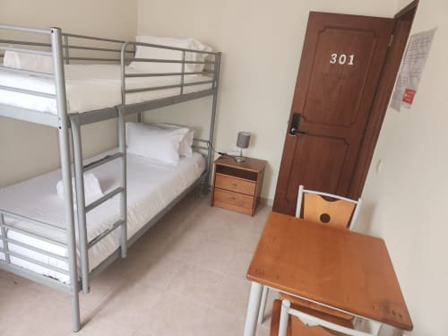 Quarto 301 do albergue Sunny House em Lagos com beliches, roupa de cama branca, escrivaninha de madeira, mesinha de cabeceira e porta marrom