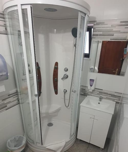 Moderno box de chuveiro com portas de vidro e puxadores de madeira no banheiro da pousada Sunny House Lagos