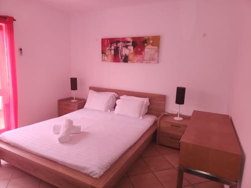 Quarto rosa na pousada Sunny House em Lagos com cama de casal, criados de madeira, caixas de som e iluminação neon