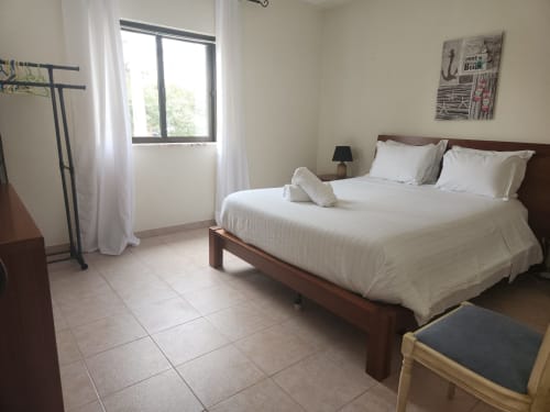 Espaçoso quarto duplo em Sunny House hostel em Lagos com cama de madeira, roupas brancas, vista para a cidade e piso cerâmico