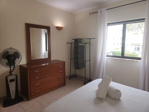 Quarto duplo ensolarado no hostel Sunny House em Lagos com cômoda de madeira, espelho, ventilador, cabideiro e vista para a cidade